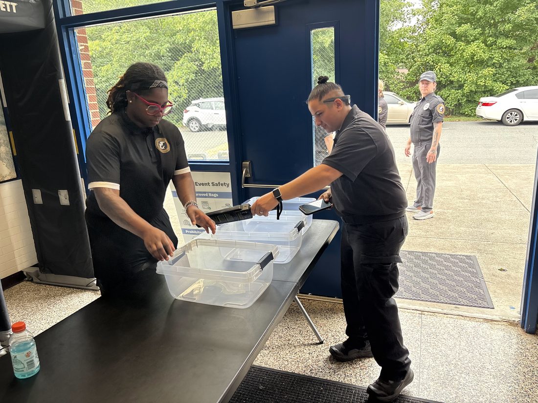 Officers staffing a bag-check and screening table at a venue entrance